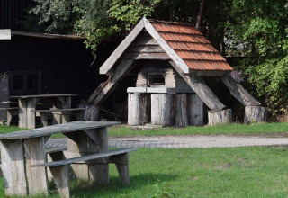Houten picknicktafels en banken buiten, naast een bakstenen oven met pannendak, in een park in Zeeland.