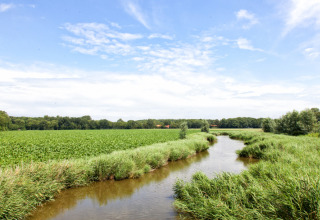 Landschap met een rivier en groene velden onder een blauwe hemel bij Feather Down Hoeve Zeeland, Zeeland.