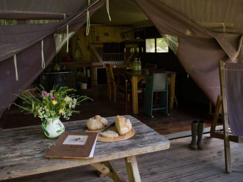 Rustic tent interior at Feather Down Hilserhof with bread, wildflowers, and wooden furniture.