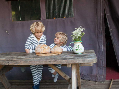 To børn i stribede pyjamas sidder ved et bord med brød og en vase blomster på Feather Down Hilserhof.