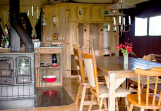Intérieur en bois chaleureux avec table à manger, poêle et fleurs, pris à Feather Down Hilserhof, Allemagne.