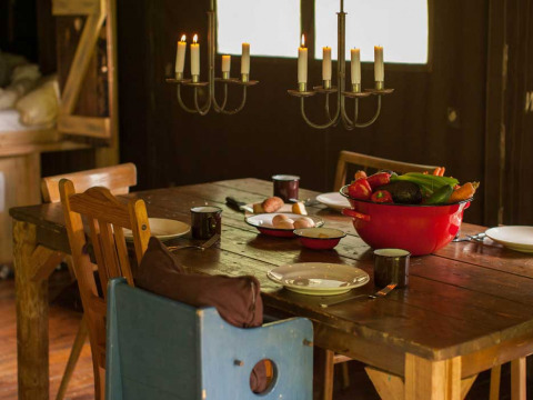 Mesa de comedor rústica con sillas de madera, candelabro y verduras frescas en bol rojo en Feather Down Hilserhof.