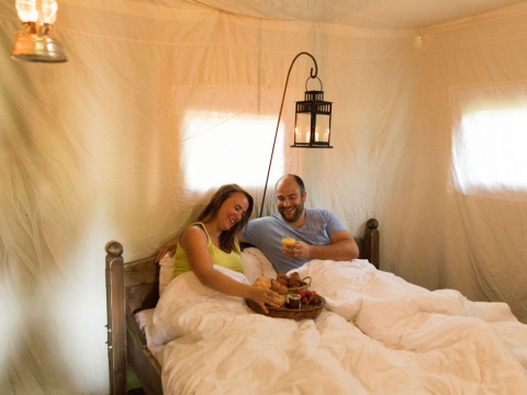 Couple enjoys breakfast in bed inside a cozy tent at Feather Down Hilserhof, Baden-Württemberg, Germany.