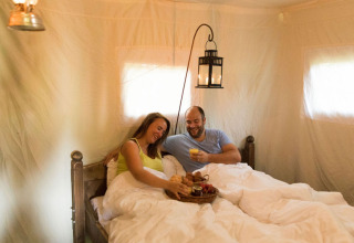 Couple enjoys breakfast in bed inside a cozy tent at Feather Down Hilserhof, Baden-Württemberg, Germany.