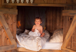Bambino sorridente seduto su un letto accogliente in legno a Feather Down Hilserhof, Germania.