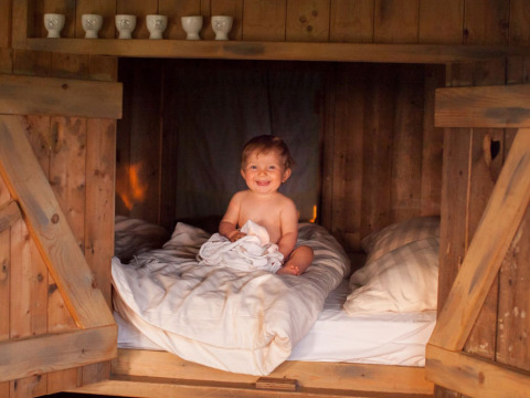 Blij kind zit op een knus houten bed bij Feather Down Hilserhof in Baden-Württemberg, Duitsland.