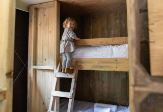 Et lille barn klatrer op ad en træstige til en køjeseng i et hyggeligt værelse på Feather Down Hilserhof.