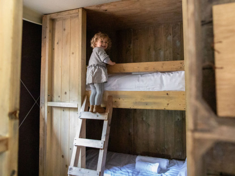 Un niño pequeño sube una escalera de madera hacia una litera en una habitación acogedora de Feather Down Hilserhof.