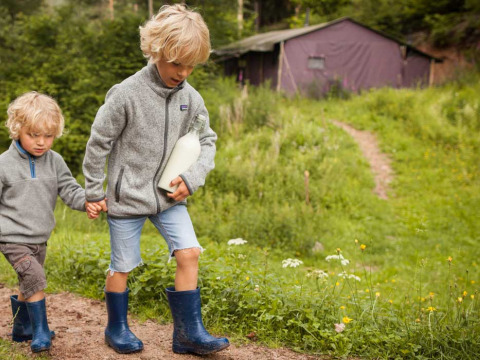 Dos niños con chaquetas grises y botas caminan con una botella de leche en Feather Down Hilserhof, Alemania.