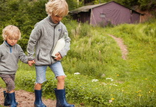 Twee kinderen in grijze truien en laarzen lopen met melk bij Feather Down Hilserhof, Duitsland.