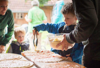 Enfants et adultes préparent des pizzas maison en plein air à Feather Down Hilserhof, parc de vacances en Allemagne.