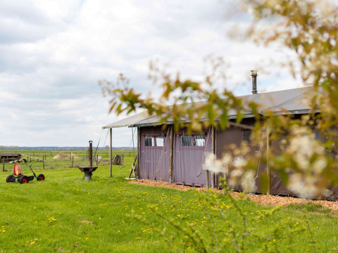 View of a tent at Feather Down De Kalverweide holiday park in Overijssel, Netherlands, with green fields.