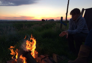 Person sidder ved et lejrbål ved solnedgang på Feather Down De Kalverweide i Overijssel, Holland.