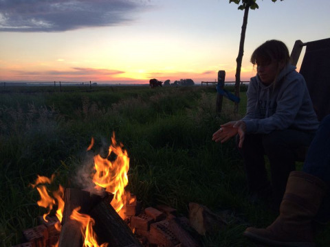 Person sitting by a campfire during sunset at Feather Down De Kalverweide in Overijssel, Netherlands.