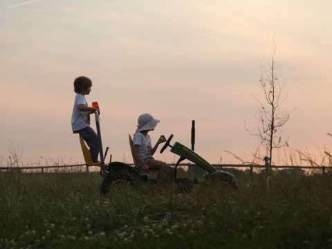 Deux enfants jouent sur un tracteur à pédales au coucher du soleil à Feather Down De Kalverweide, Overijssel, Pays-Bas.