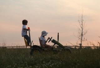 Twee kinderen fietsen op een traptractor bij zonsondergang, Feather Down De Kalverweide, Overijssel, Nederland.