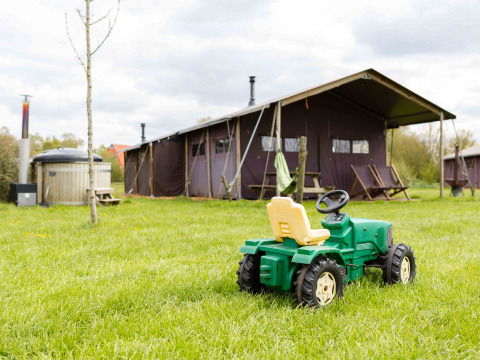 Tractor de juguete sobre césped frente a tienda glamping en Feather Down De Kalverweide, Overijssel, Países Bajos.