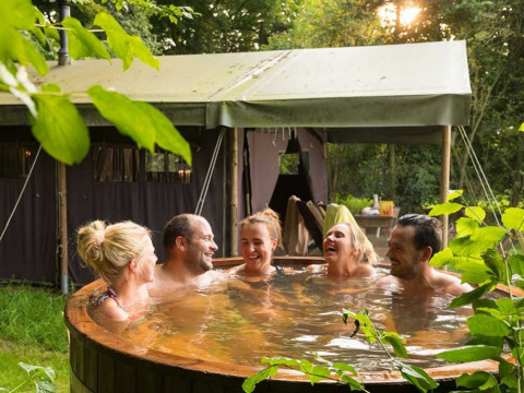 Vijf personen ontspannen in een hottub voor een tent bij Feather Down De Kalverweide, Overijssel.