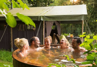 Five people relaxing in an outdoor hot tub in front of a tent at Feather Down De Kalverweide, Netherlands.