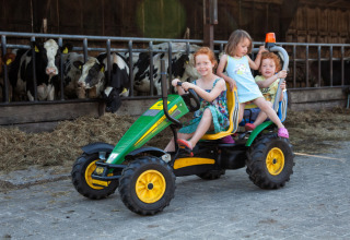 Drie kinderen op een groene traptractor bij een koeienstal in Feather Down De Kalverweide, Overijssel.