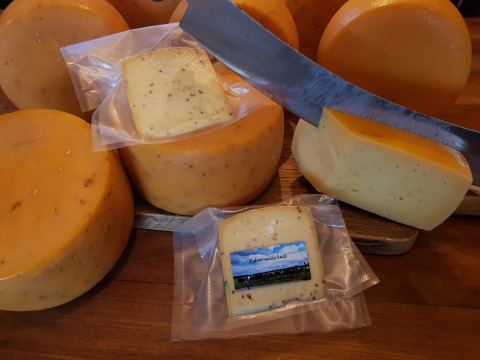 Ruedas de queso y lonchas envasadas al vacío sobre tabla de madera, en Feather Down De Kalverweide, Países Bajos.