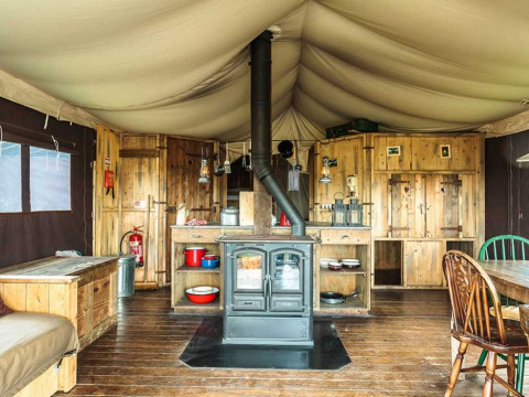 Interior de tienda rústica con estufa de leña y muebles de madera en Feather Down Glastonbury Hill Farm, Inglaterra.