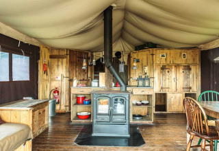 Interiør af rustik teltlodge med brændeovn og træmøbler på Feather Down Glastonbury Hill Farm, England.
