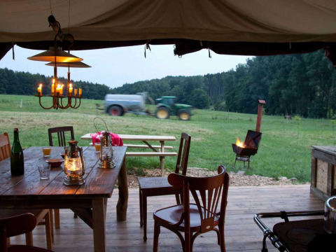 Vista desde una tienda con mesa rústica, linternas, fogata y tractor en Glastonbury Hill Farm, Inglaterra.