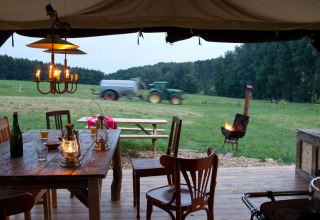 Blick aus einem Zelt mit rustikalem Tisch, Laternen, Feuerstelle und Traktor auf Glastonbury Hill Farm.