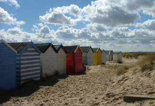Kleurrijke strandcabines op het zand aan Feather Down College Farm, Oost-Engeland, onder een wolkenlucht.