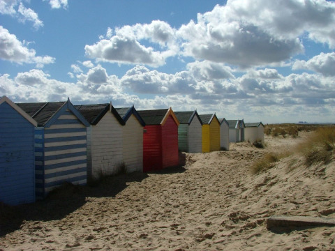 Kleurrijke strandhuisjes op het zand bij Feather Down College Farm, Oost-Engeland, onder een bewolkte lucht.