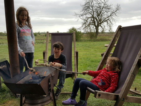 Trois enfants grillent du pain sur un feu de camp à Feather Down College Farm, Est de l’Angleterre, Royaume-Uni.