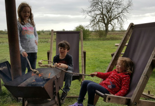 Drie kinderen roosteren brood boven een kampvuur bij Feather Down College Farm in Oost-Engeland, VK.