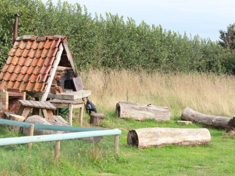 Buitenruimte met boomstammen als zitplaatsen en bakstenen hut met pannendak op Feather Down College Farm.