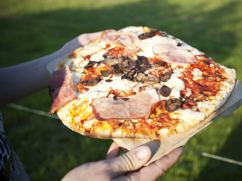 Iemand houdt buiten een pizza met ham, champignons en kaas op Feather Down Fountain Violet Farm, Zuidwest-Engeland.