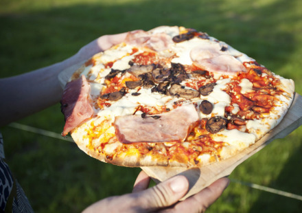 Iemand houdt een pizza met ham, champignons en kaas buiten bij Feather Down Fountain Violet Farm in Zuidwest-Engeland.