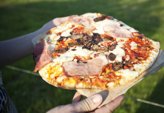 Una persona tiene una pizza con prosciutto, funghi e formaggio all'aperto alla Feather Down Fountain Violet Farm, Regno Unito.