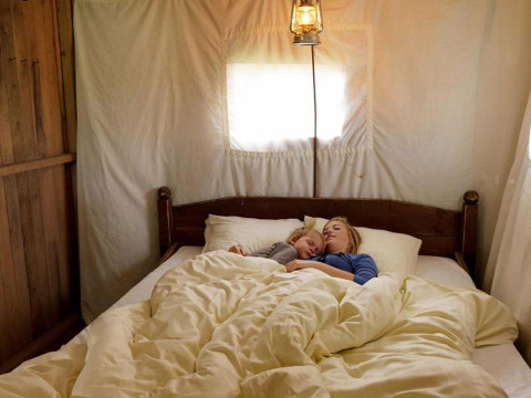 Zwei Menschen schlafen gemeinsam in einem Bett unter einer Laterne in einer Glamping-Unterkunft im Ferienpark.