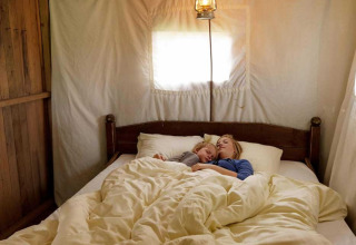 Dos personas duermen juntas en una cama bajo una linterna en una tienda glamping de un parque vacacional.
