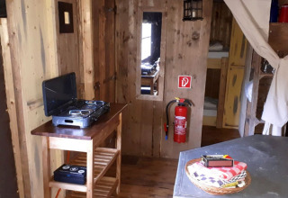 Rustic wood interior with gas stove, fire extinguisher, and bed area at Fountain Violet Farm, England.
