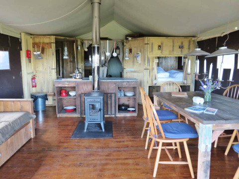 Gezellige tentinrichting op Feather Down Fountain Violet Farm met houten tafel, stoelen en kachel.