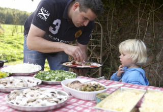 En mand og et barn laver pizza udendørs på Feather Down Fountain Violet Farm med friske ingredienser.