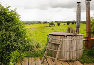 Rustiek houten hottub met ladder bij Feather Down Hollings Hill, met uitzicht op groene weilanden in VK.
