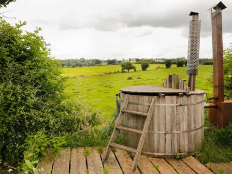Rustiek houten hottub met ladder bij Feather Down Hollings Hill, met uitzicht op groene weilanden in VK.