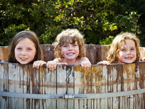 Drie blije kinderen in een houten bad bij Feather Down Hollings Hill vakantiepark in West Midlands, Verenigd Koninkrijk.