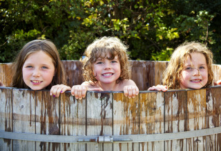 Three smiling children enjoy a wooden hot tub at Feather Down Hollings Hill holiday park in West Midlands, UK.