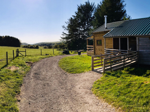 Camino de grava junto a una cabaña de madera en Feather Down Warren Farm, Suroeste de Inglaterra, con campos verdes.