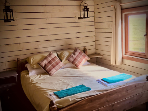 Accogliente camera da letto con letto matrimoniale, cuscini a quadri e finestra a Feather Down Warren Farm nel sud-ovest dell’Inghilterra.