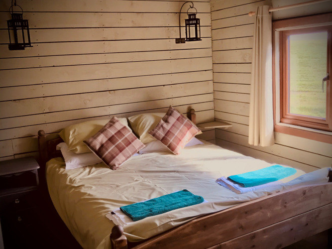 Gezellige slaapkamer met tweepersoonsbed, geruite kussens en raam bij Feather Down Warren Farm in Zuidwest-Engeland.