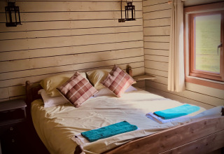 Knusse slaapkamer met tweepersoonsbed, ruitkussens en raam op Feather Down Warren Farm in Zuidwest-Engeland.